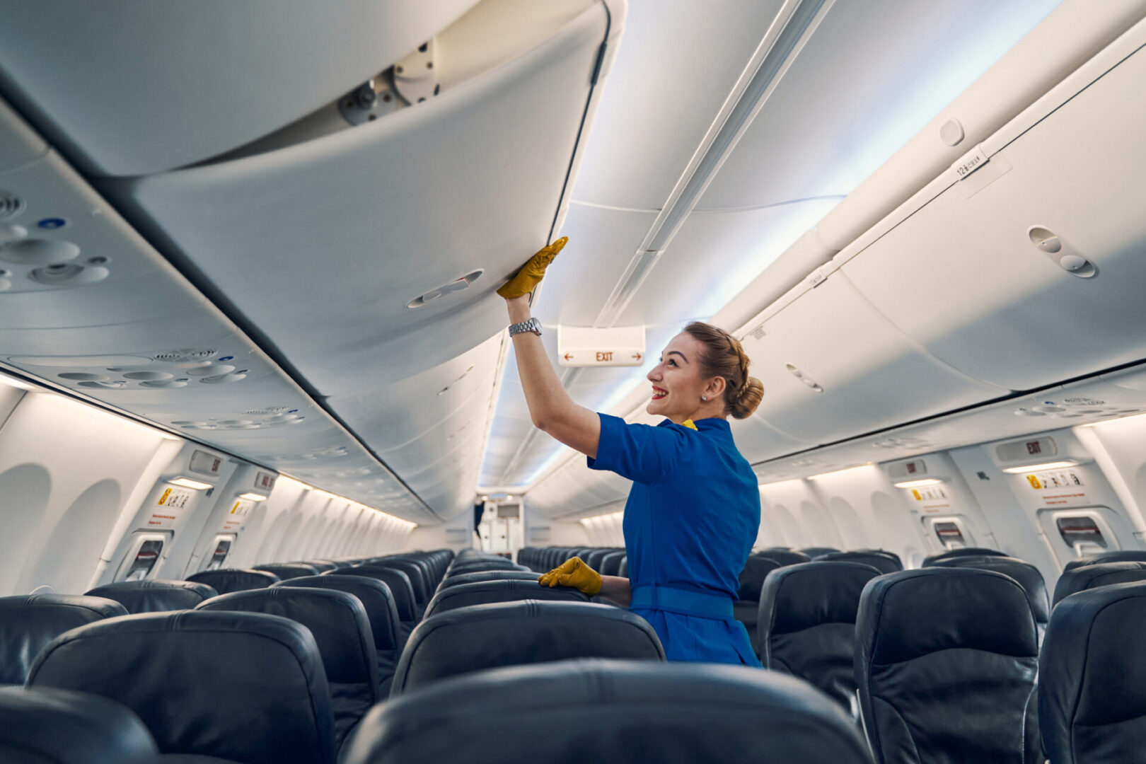 Flight attendant organizing airplane overhead compartment.